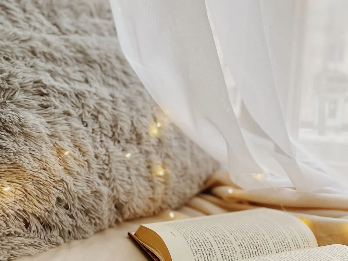 Un livre est ouvert sur un sofa pelucheux près d'une fenêtre ouverte.