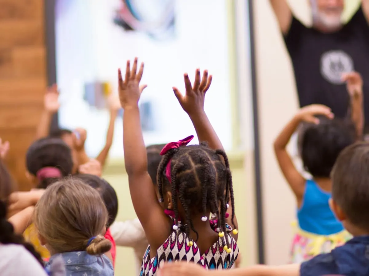 Des enfants qui participent à une activité et qui lèvent les bras dans les airs.