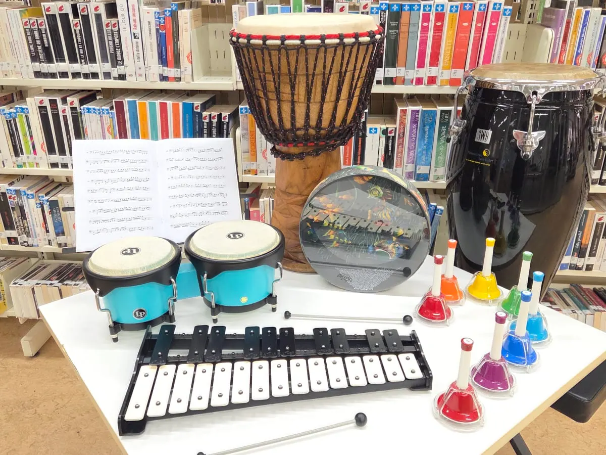 Des instruments de musique sont disposés sur une table en face d'une étagère pleine de livres.