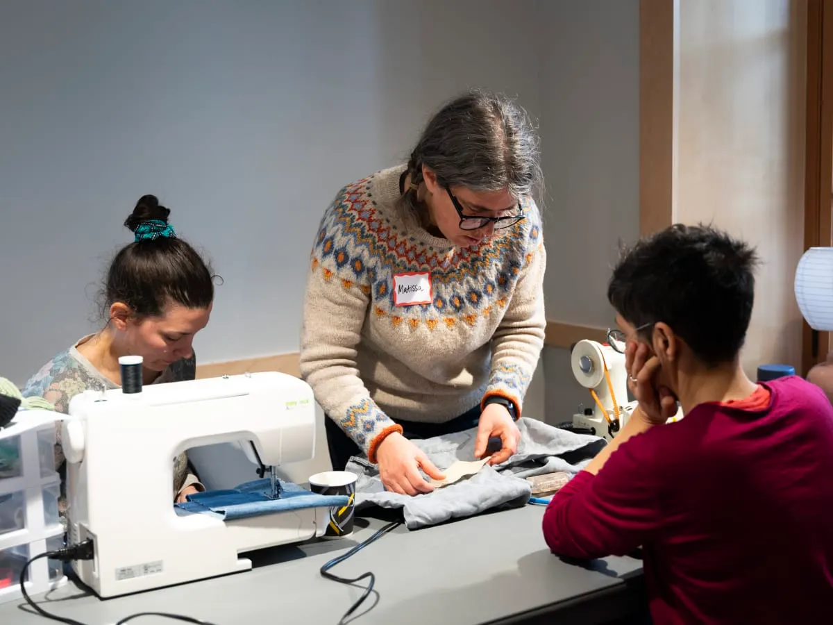 Trois femmes concentrées dans un atelier de couture et de réparation.