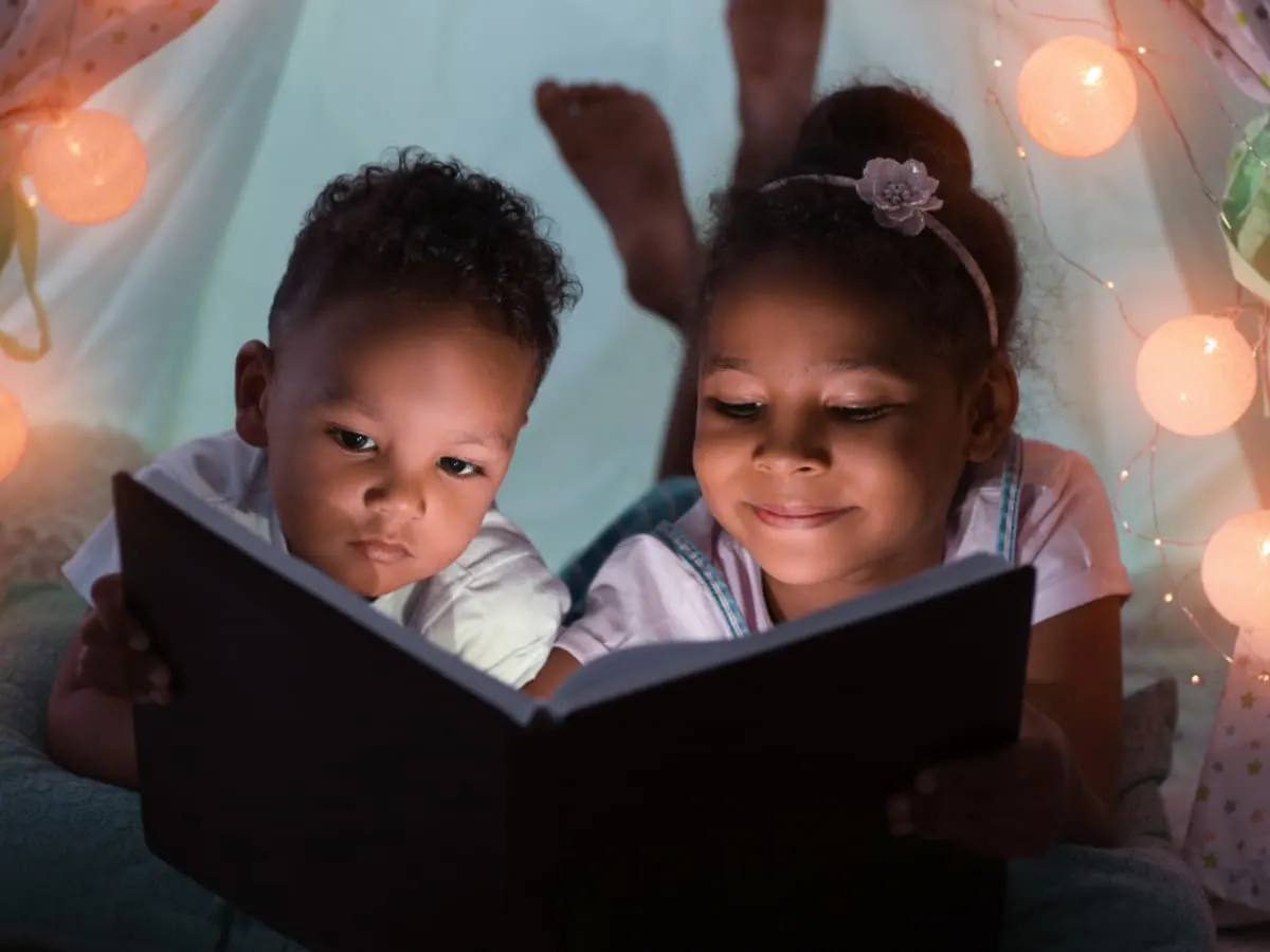 Photo d'enfants lisant un livre en pyjama entourés d'une guirlande de lumières