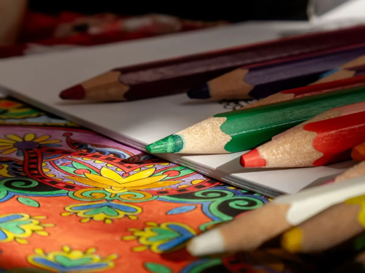 Cette image est une photographie en gros plan d'un espace de coloriage et de création artistique. Plusieurs crayons de couleur sont dispersés.