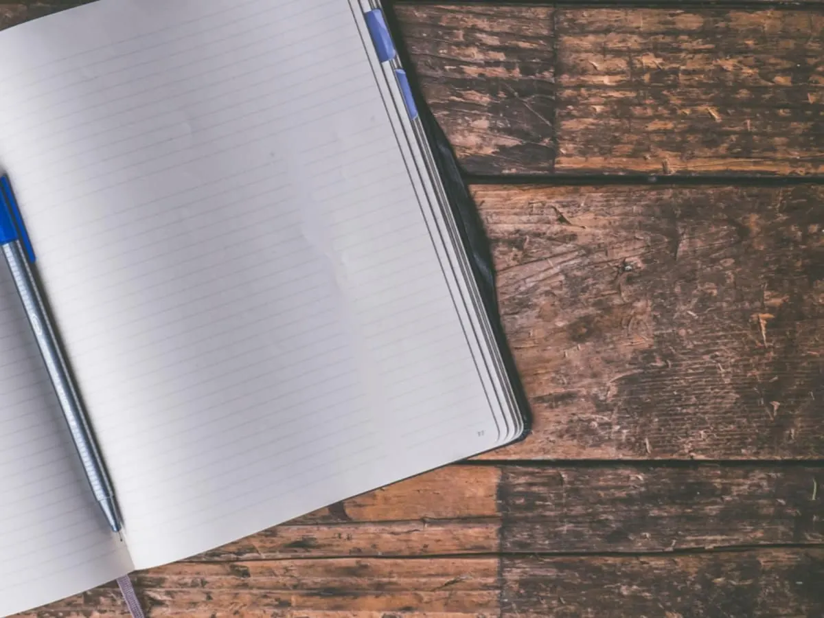 Un carnet ouvert avec un crayon au centre, posés sur une table en bos.