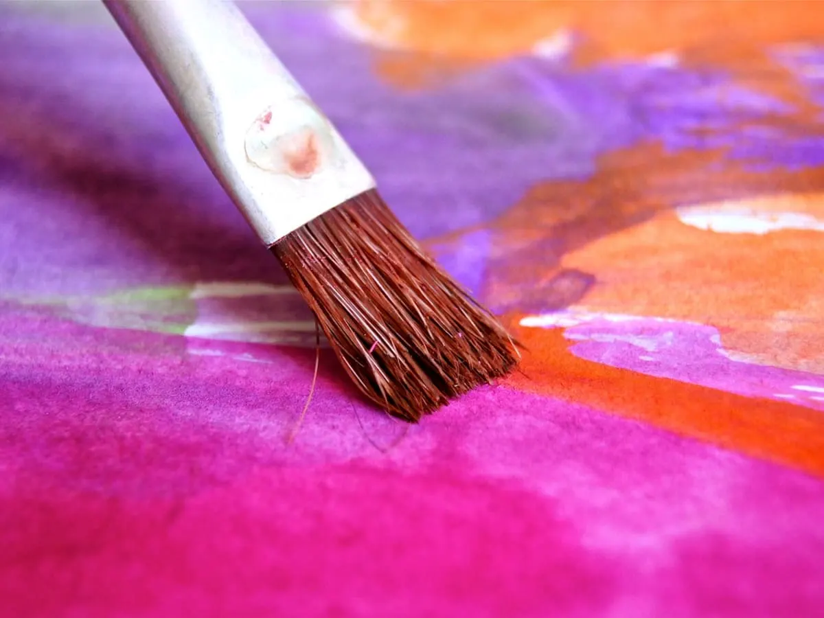 Un pinceau sur une feuille peinte de différentes couleurs.