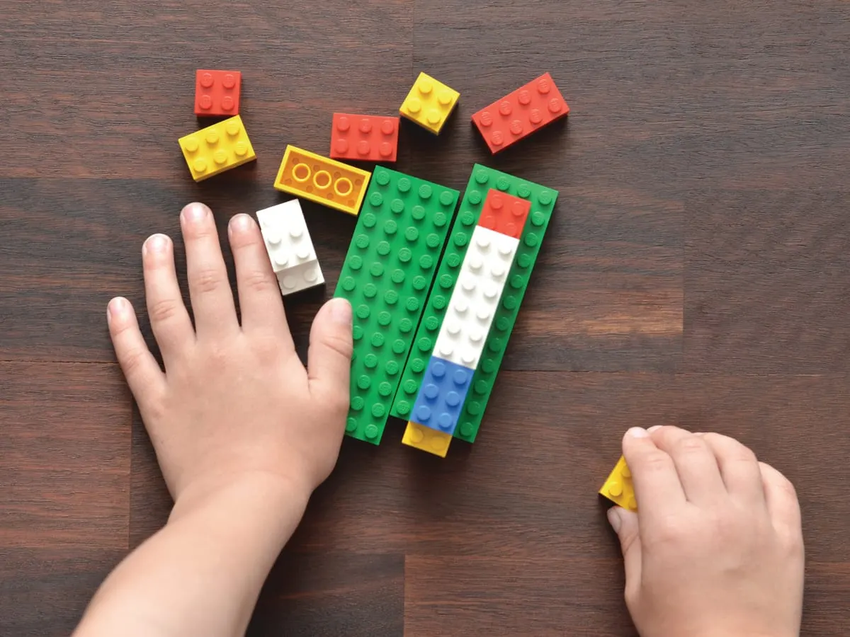 Blocs de Lego de différentes couleurs avec une main qui les manipule.