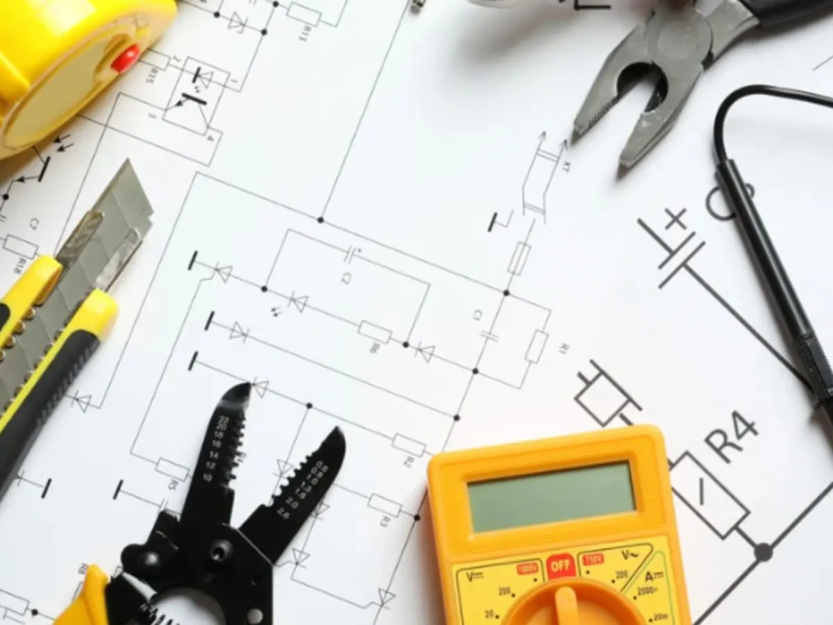 Illustration montrant des outils et instruments de mesure disposés sur un plan de circuit électrique. L’image évoque une activité de découverte de l’électricité, de l’électronique et du fonctionnement des circuits.