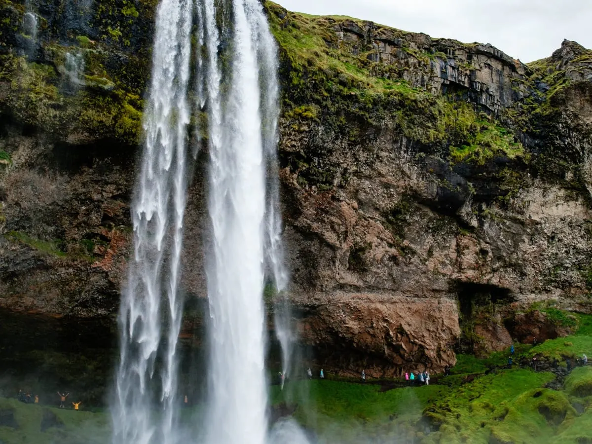 Cette image montre un paysage naturel spectaculaire dominé par une grande chute d'eau qui se déverse du sommet d'une falaise rocheuse.
