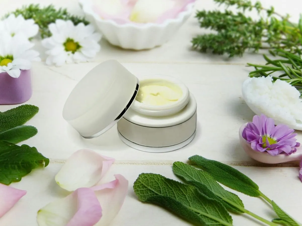 Un petit pot de produit de beauté entouré de plantes et de fleurs.