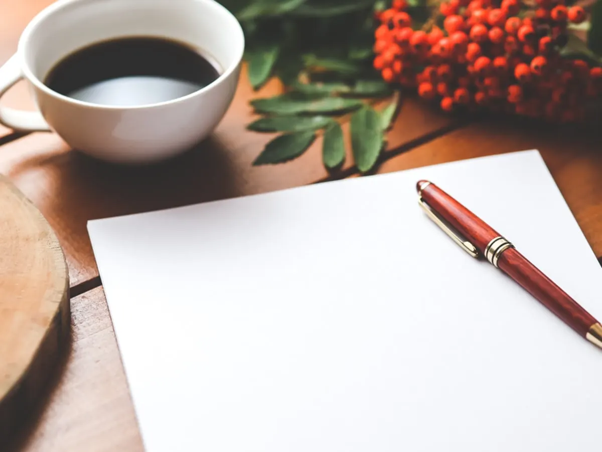 Une page blanche et un crayon, posés sur une table près d'une tasse de café.