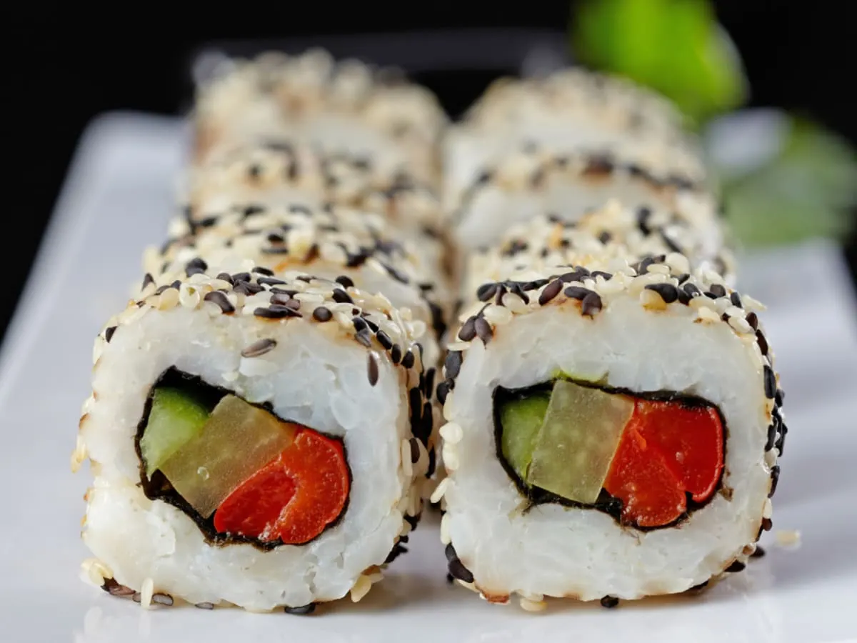 Gros plan sur des sushis végétariens garnis de riz, de légumes colorés et de graines de sésame, soigneusement disposés sur un plateau. L’image met en valeur une activité culinaire créative et conviviale autour de la découverte de saveurs végétales.