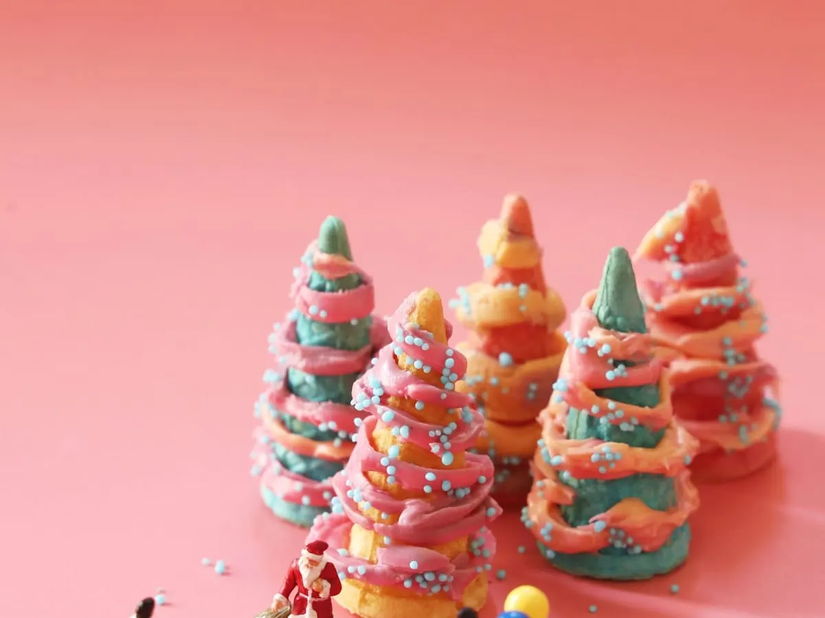 Cette image présente une scène miniature créative sur un fond rose pastel. L’ensemble évoque une ambiance festive et féerique inspirée de la période des fêtes.