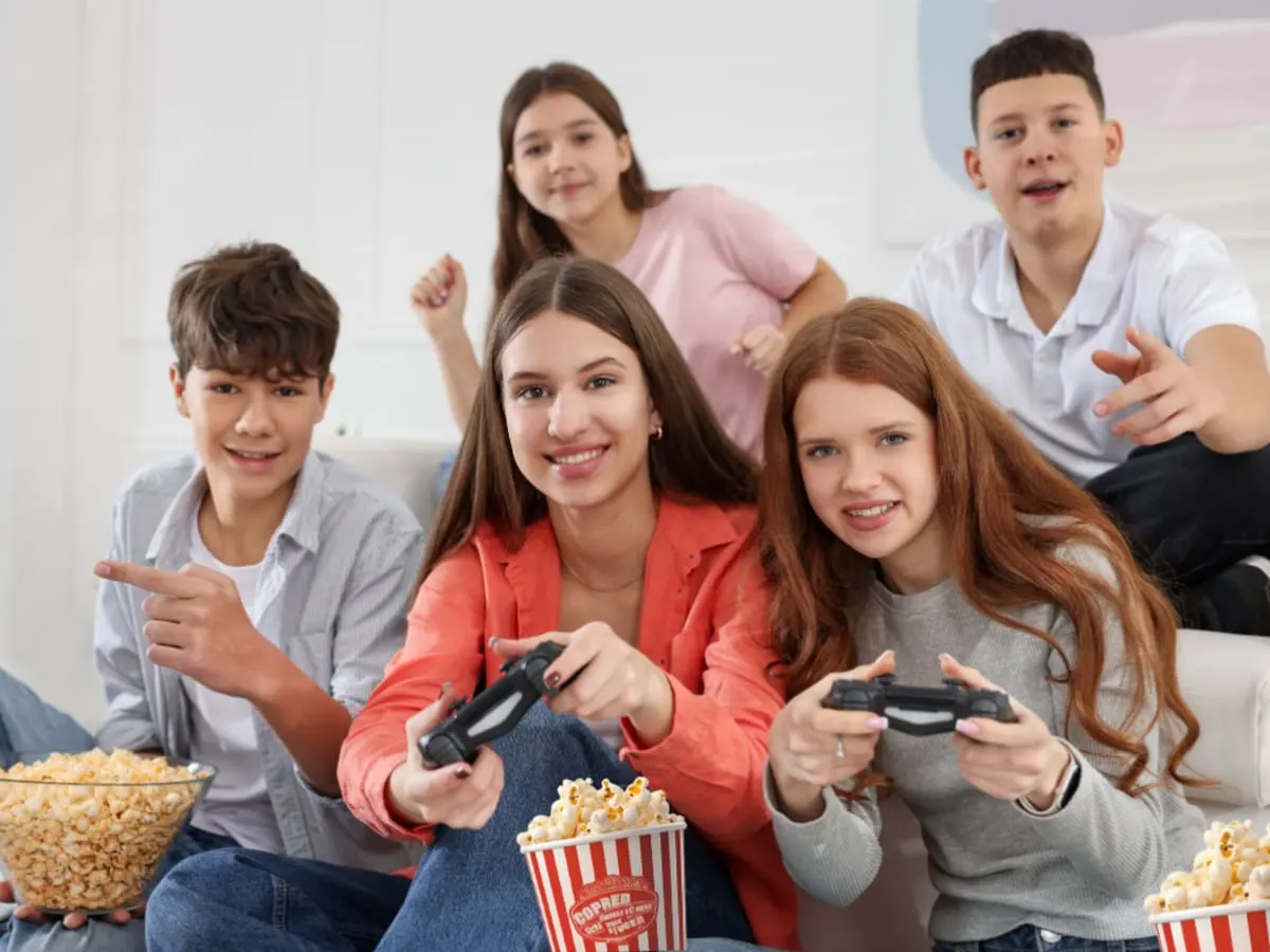 Un groupe d'ados joue à des jeux vidéo en mangeant du popcorn.