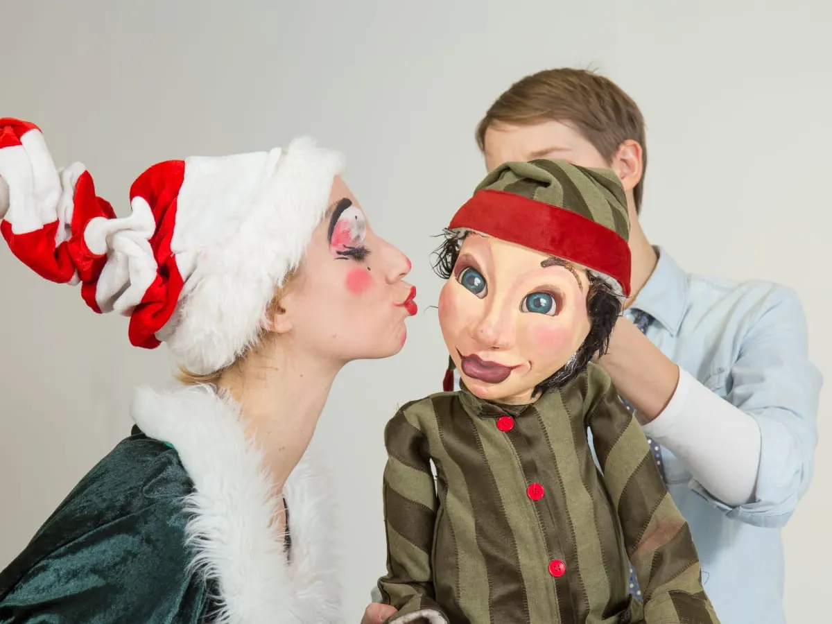 un personnage déguisé en lutin embrasse sur la joue une marionnette