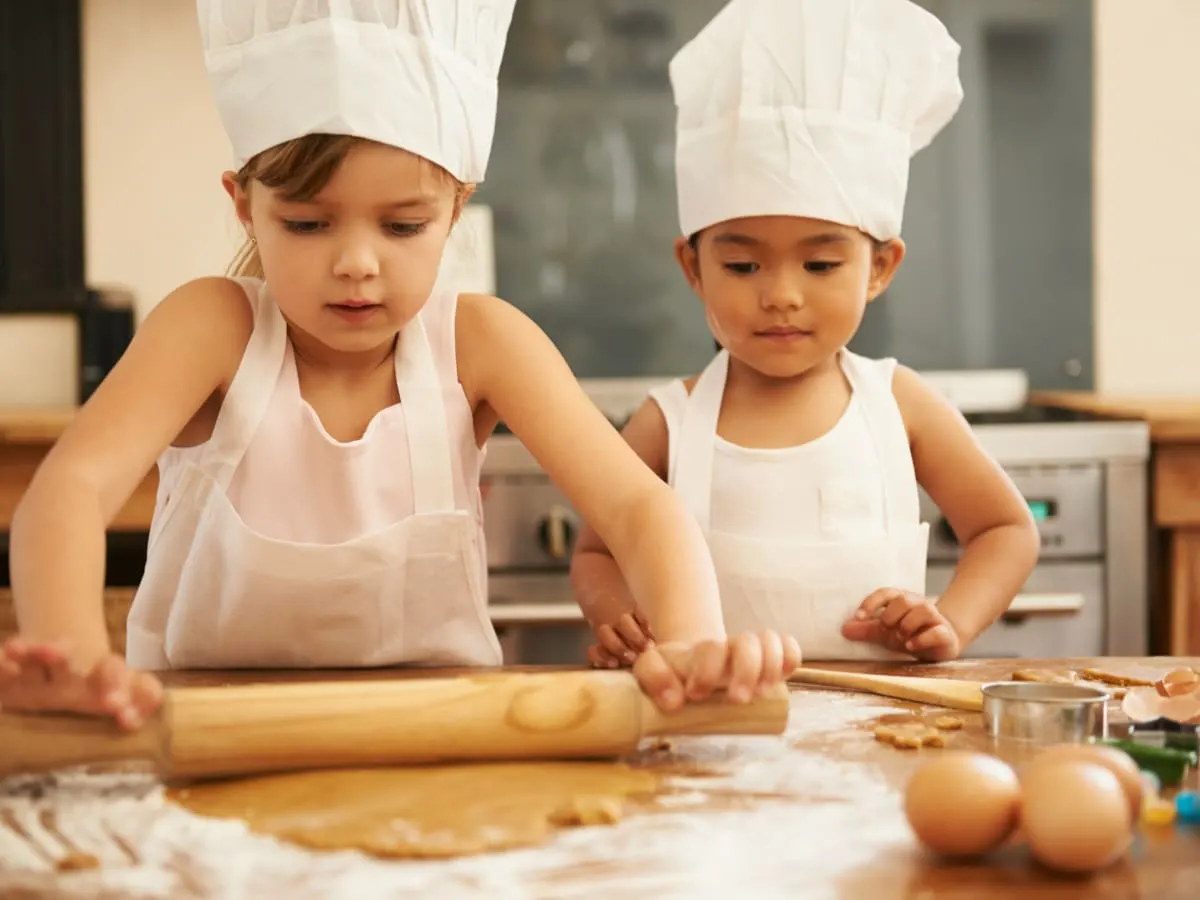 Photographie de deux enfants avec toque de chef cuisiner en train d'étaler de la pâte